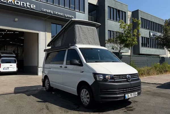 Beyaz VW Transporter T6 Cappadocia — Demonte Caravan tesisi önünde, SCA açılır tavan açık
