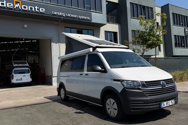 Beyaz VW Transporter Efes — Demonte Caravan üretim tesisi önünde, SCA ters açılır tavan ve güneş paneli