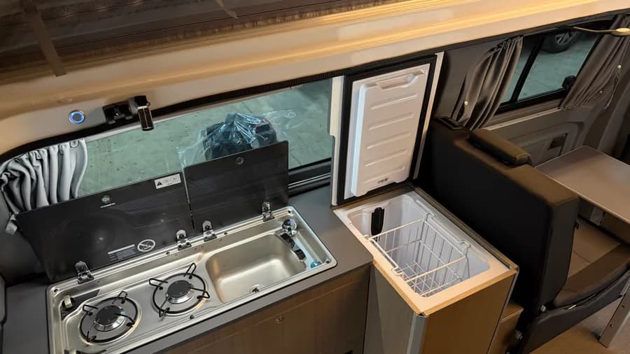 Küchendetail mit Dometic-Kocher und Spüle sowie geöffnetem Indel-B-Kompressorkühlschrank