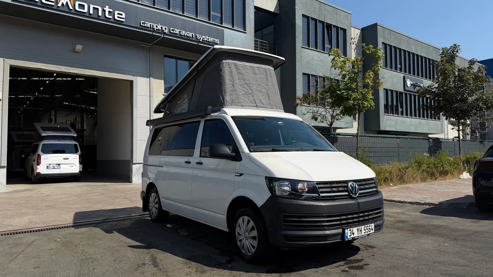Weißer VW Transporter T6 Cappadocia vor dem Demonte-Caravan-Werk mit ausgestelltem SCA-Dach