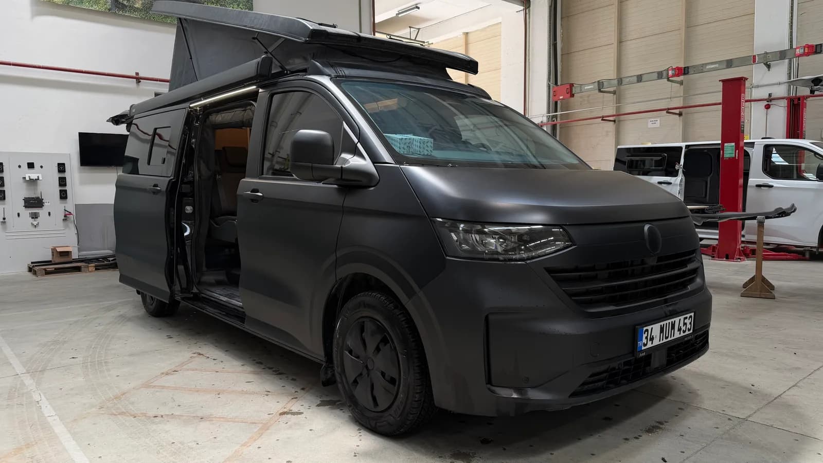 Mattschwarzer Volkswagen Transporter 4x4 Olympos in der Werkstatt mit geöffnetem SCA-Aufstelldach und offener Schiebetür
