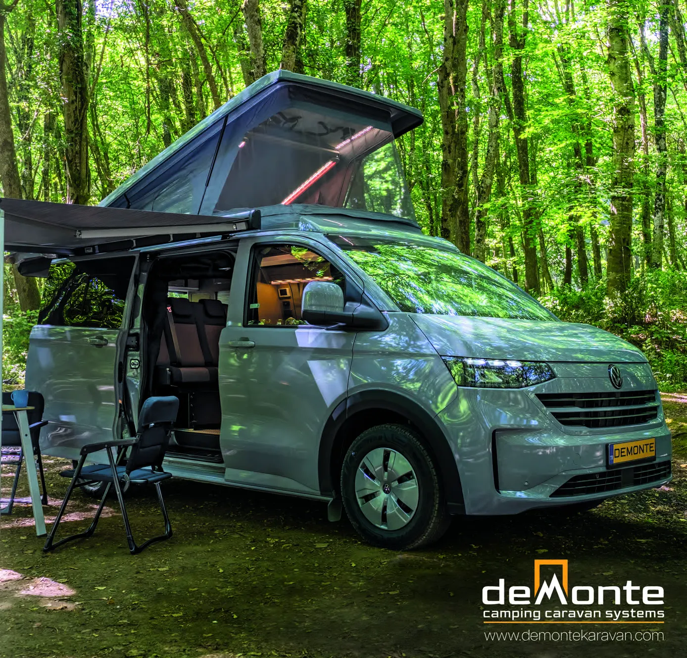 Demonte Karavan Katalog 2026, Seite 1: Titelseite — ein VW Transporter im Wald mit geöffnetem Aufstelldach und Markise, daneben ein Campingstuhl